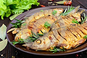 Fried fish carp sazan on a ceramic bowl with branches of rosemary