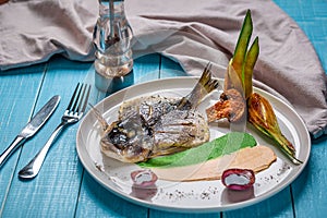 Fried fish dorado, decorated with cucumbers and onions. On a blue wooden background