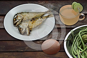Fried fish, eggs, fresh vegetables and lemon juice on wooden background