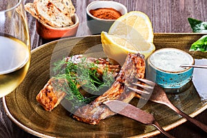 Fried fish fillet with cheese sauce, greens and lemon on plate on wooden background. Hot fish dish.