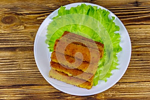 Fried fish fingers on plate with lettuce on wooden table. Top view