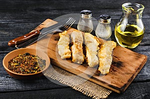 Fried fish in fried fish fillet pangasius on a wooden cutting board with spices, fork and knife on a black wooden background