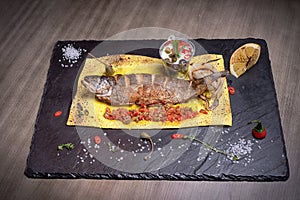 Fried fish on a leaf of lavash with onions, lemon, red pepper and salt and vegetable cut. For the menu of cafe. wooden