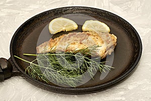 fried fish with lemon and herbs in a frying pan on the table