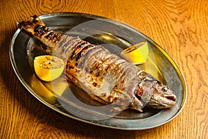 Fried fish lying on a black plate with vegetables and lemon