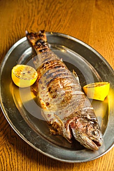 Fried fish lying on a black plate with vegetables and lemon