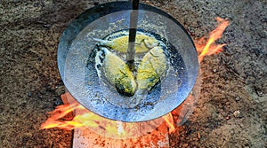 Fried fish prepared on metallic disk as grilling food. Camping food prepared on grill installation