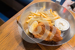 Fried fish steak served with french fries and tartar sauce in a deep pan placed