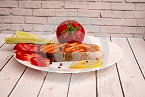 Fried fish steak on a white plate with tomatoes, onions, cucumbers, on the boards