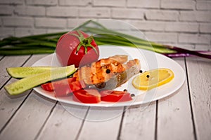 Fried fish steak on a white plate with tomatoes, onions, cucumbers, on the boards