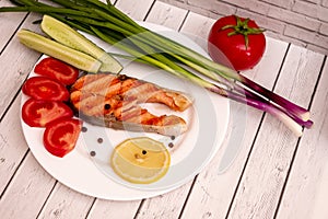 Fried fish steak on a white plate with tomatoes, onions, cucumbers, on the boards