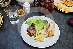 Fried fish,vegetable,lettuce and potoato salad on table with drink and food.