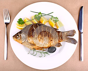 Fried fish on white plate with fork and knife