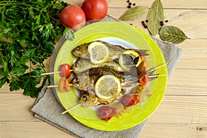 Fried fish (carp) on skewers with pieces bell pepper, sun-dried tomatoes and lemon.