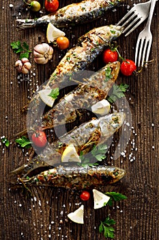 Fried fishes with addition of herbs, spices and lemon slices on a wooden background