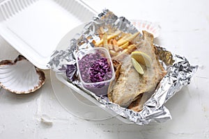 Fried flounder fillet served with fries and red cabbage salad, in a takeaway box, on a white background. Fish and chips.