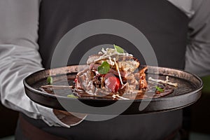 fried foie gras with cherry tomatoes on a dark plate held by a waiter in his hand