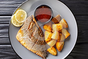 Fried gilt-head fish fillet with a side dish of potatoes and sauces close-up on a plate. Horizontal top view