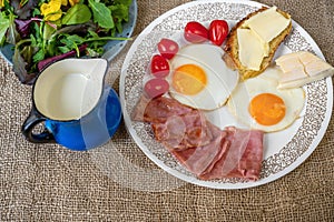 Fried ham and eggs, cherry tomato, bread with butter, cheese, blue pitcher with milk and salad, breakfast