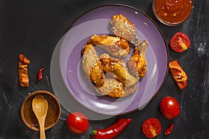 Fried juicy chicken wings marinated with honey, soy sauce, spices, sprinkled with sesame seeds on a plate on a black