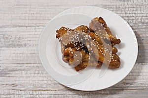 Fried juicy chicken wings marinated with honey, soy sauce, spices, sprinkled with sesame seeds on a white plate on a