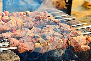 Fried and juicy meat with mushrooms is fried on skewers on a fire, skewers on bricks, under them burning wood coals. Fried meat an