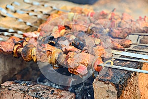 Fried and juicy meat with mushrooms is fried on skewers on a fire, skewers on bricks, under them burning wood coals. Fried meat an