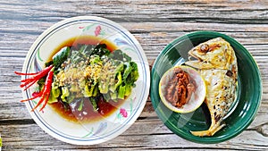 Fried kale vegetables with fried big mackerel served as lunch on the table look tasty.