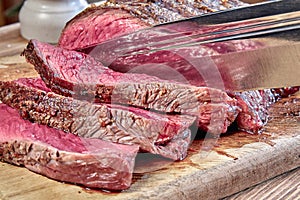 Fried meat with blood is cut with hunting knife. Well done steak closeup on wooden background. Rustic style.