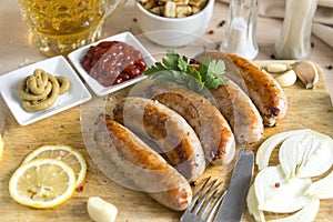 Fried meat sausages on cutting Board, ketchup, mustard, onion, greens, lemon, garlic, light beer mug