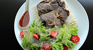 Fried meat and spicy sauce served on plate with lettuce leaves and thin bread