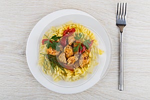 Fried meat with sweet pepper, fusilli in plate, fork