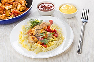 Fried meat, sweet pepper, fusilli in plate, mayonnaise, ketchup, fork