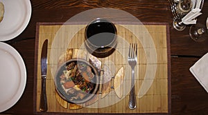 Fried meat and waxes on a dark frying pan on a wooden stand.