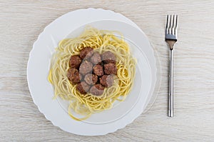 Fried meatballs with spaghetti in dish, fork on wooden table. Top view