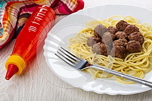 Fried meatballs with spaghetti, fork in dish, bottle with ketchup, napkin on wooden table