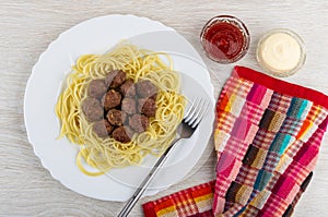 Fried meatballs with spaghetti, fork in dish, bowls with ketchup and mayonnaise, napkin on wooden table. Top view