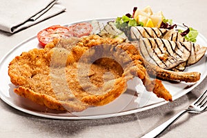 Fried Milanese cotoletta with tomatoes on plate