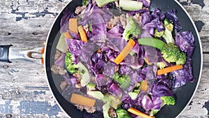 Fried mixed vegetables in a pan and wood background