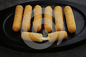 Fried mozzarella sticks crispy on a black woden plate isolated - close up