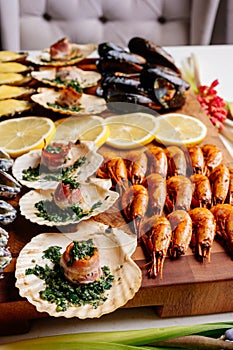 Fried mussels in shells and baked scallops in shell with bacon and sliced lemon on wooden cutting