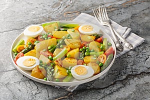 Fried new potatoes with asparagus, cherry tomatoes, boiled egg and green peas close-up in a plate. Horizontal