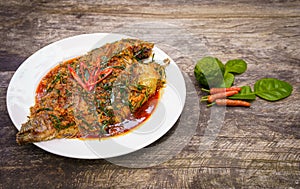 Fried Nile tilapia fish with red curry paste on white plate wooden background, Thai food is spicy mixed with sweet flavor with