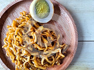 Fried noodles with boiled egg pieces on a wooden plate