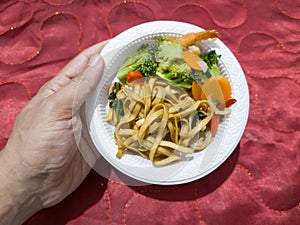 Fried noodles in a white plate with sliced ??toppings and green vegetables