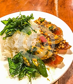 Fried one-thousand-year egg with crispy holy basil leaves and rice dish on a wood table. Spicy popular traditional Thai authentic