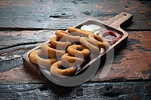 Fried onion rings with ketchup and mayonnaise on rustic wooden table