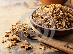 Fried onions in bowl on wooden background with wooden spoon
