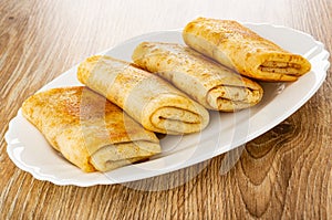 Fried pancake rolls with filling in white dish on wooden table