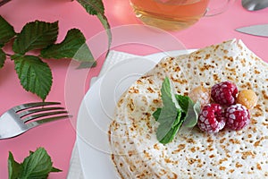 Fried pancakes close-up on a white plate, pancakes with raspberries, tea cerimonia, dessert on a pink background